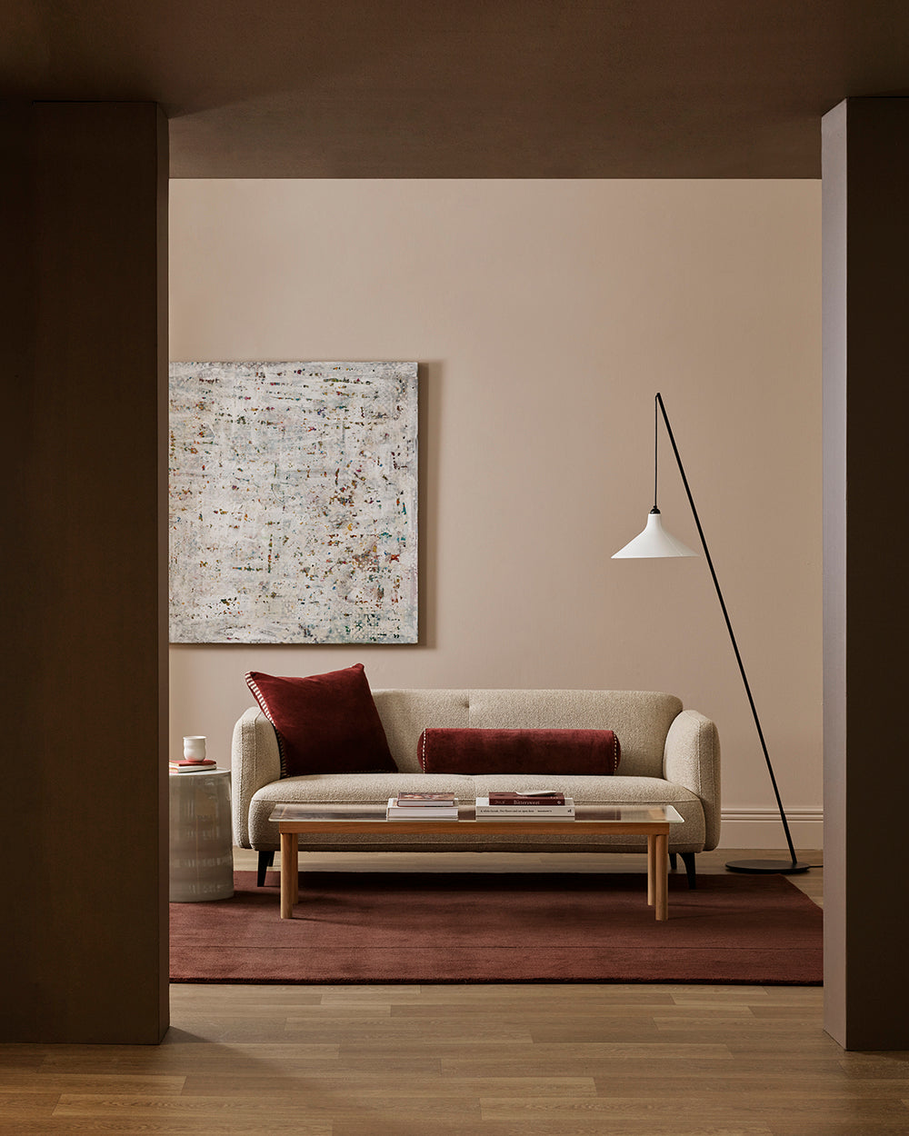 Baya Elliot cotton velvet bolster cushion in Oxblood, styled in a living room with a cream boucle sofa and floor lamp
