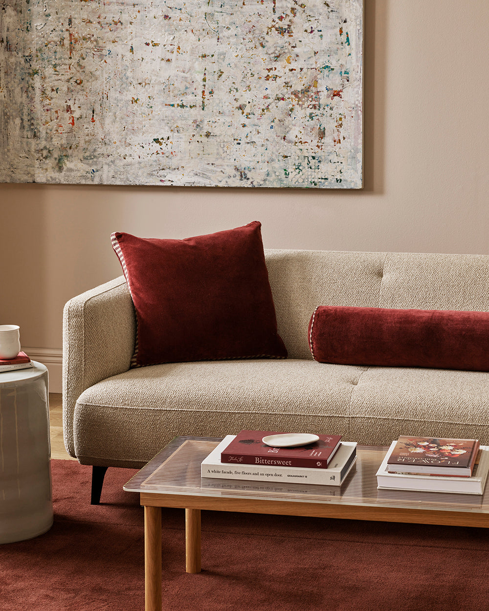 Baya Elliot cotton velvet bolster cushion in Oxblood, close view on a cream boucle sofa with a matching square cushion