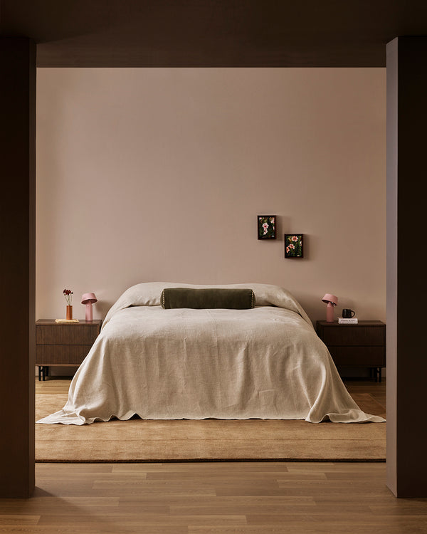 Baya Elliot cotton velvet bolster cushion in Thyme, on a bed in a styled bedroom