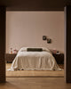 Baya Elliot cotton velvet bolster cushion in Thyme, on a bed in a styled bedroom