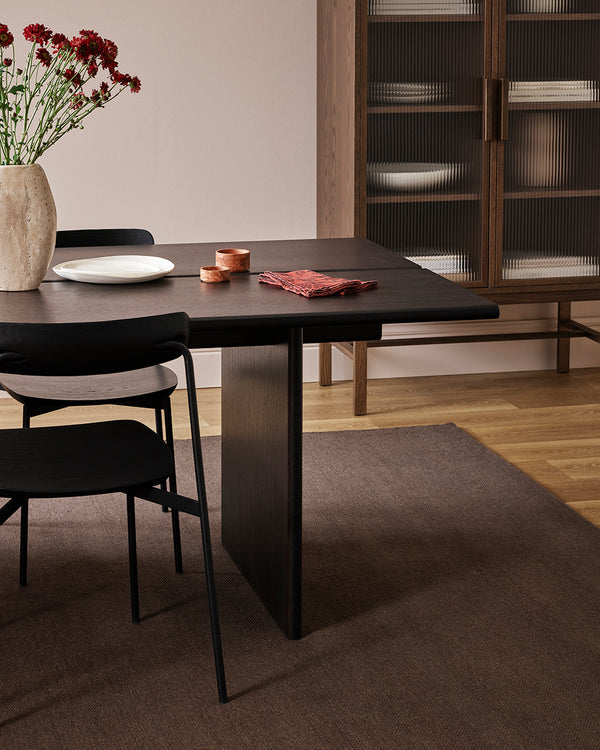 Baya Fairmont NZ Wool Floor Rug in Bracken, under a dining table with a vase of flowers and a glass-front cabinet