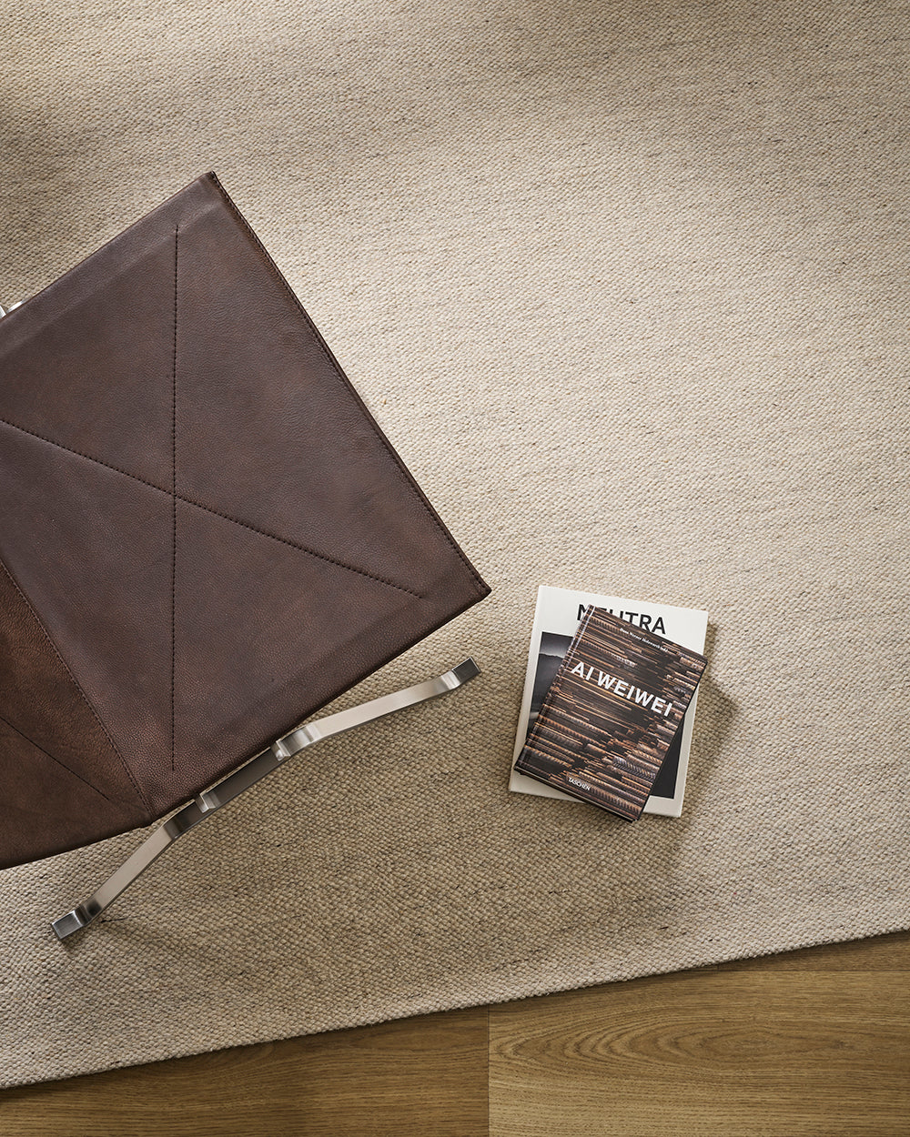 Baya Fairmont NZ Wool Floor Rug in Limestone, overhead view beside a leather chair with books