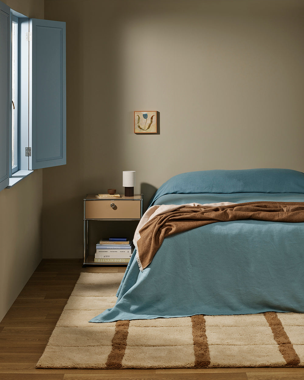 Baya Langford throw in coffee draped over a bed, in a bedroom with a pale blue shuttered window.