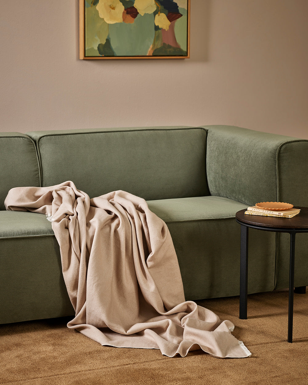 Baya Langford throw in ecru draped over a green sofa and pooling onto the floor.