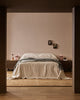 Baya Langford throw in khaki draped over a bed, seen through a doorway in a dark bedroom.