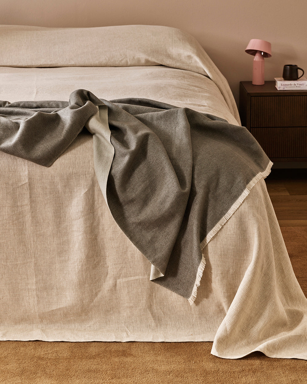 Baya Langford throw in khaki draped over a linen bedspread beside a bedside table.