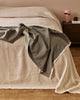 Baya Langford throw in khaki draped over a linen bedspread beside a bedside table.