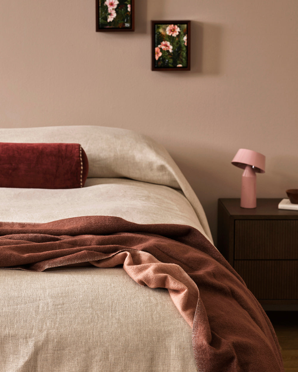Baya Langford throw in raisin draped over a bed, close view beside two framed floral prints.