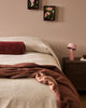 Baya Langford throw in raisin draped over a bed, close view beside two framed floral prints.