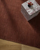 Overhead styling shot of the Baya Linden Floor Rug in Brick beneath a marble side table with a vase of red roses.