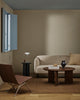 The Baya Linden Floor Rug in Ironbark styled in a living room with a beige sofa, leather armchair and round coffee table, showing its earthy brown tone.