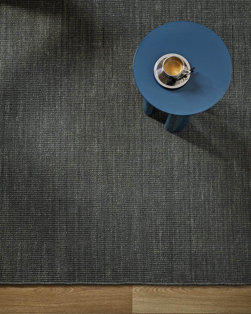 Overhead styling shot of the Baya Linden Floor Rug in Petrol beside a round blue side table with an espresso cup.