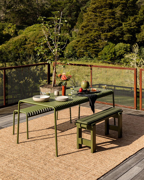 Baya Ormond outdoor rug in Biscotti, styled on a timber deck beneath a green outdoor dining table and bench.