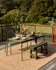 Baya Ormond outdoor rug in Biscotti, styled on a timber deck beneath a green outdoor dining table and bench.