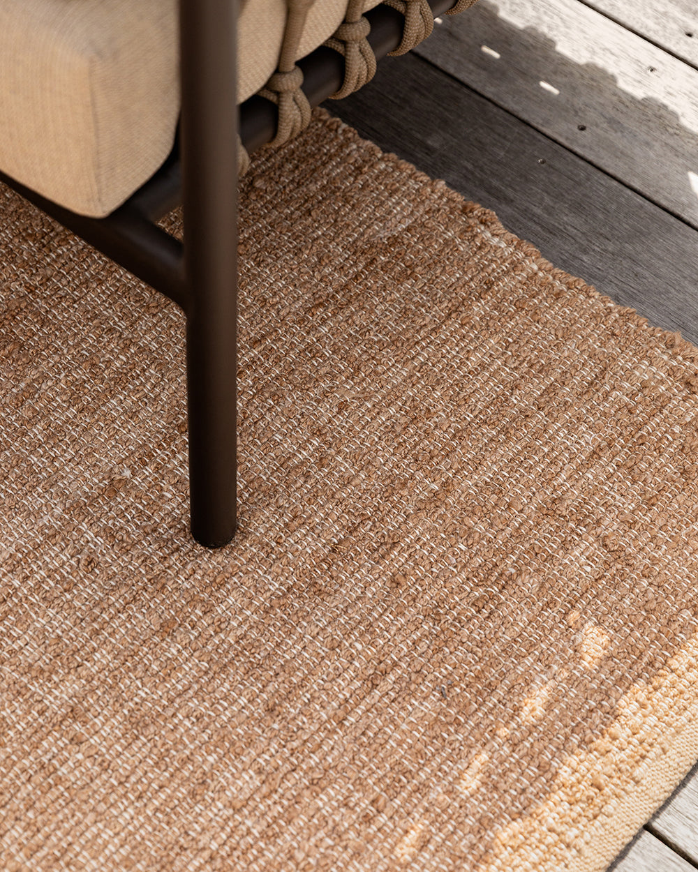 Baya Ormond outdoor rug in Biscotti, styled on a timber deck beneath an outdoor chair.