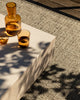Baya Ormond outdoor rug in Mineral, styled on a deck under a pale stone table with an amber glass carafe and tumblers.