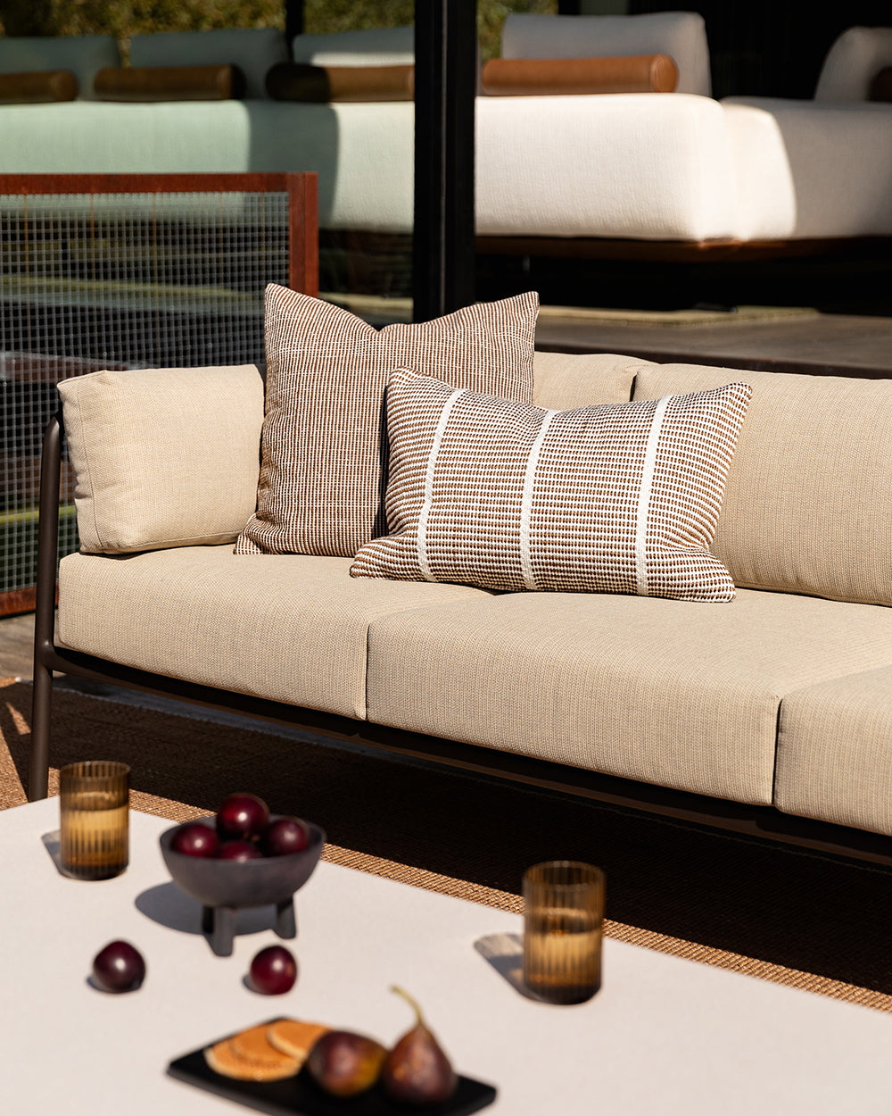 Baya Shore outdoor lumbar cushion in Tobacco styled on an outdoor sofa, with a second textured cushion in the background