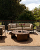 Baya Solar Outdoor Lumbar Cushion in Chocolate, styled on an outdoor sofa in full sun beside a table with fresh flowers.