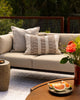 Baya Solar Outdoor Lumbar Cushion in Chocolate, styled on an outdoor sofa with a stone side table and citrus platter.