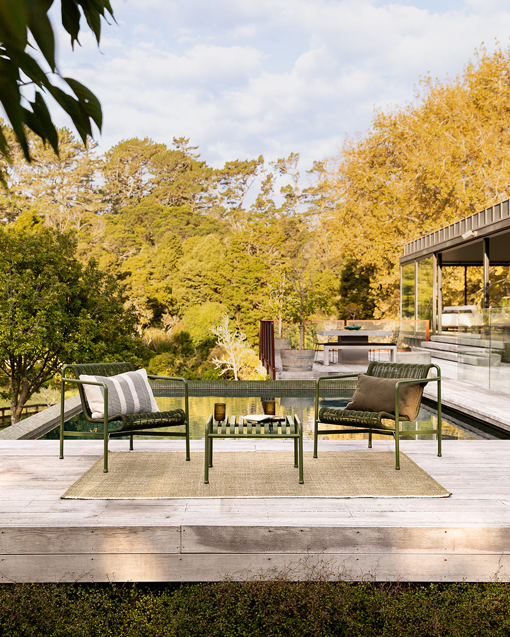 Baya Solar Outdoor Lumbar Cushion in Mangrove, styled on an outdoor sofa in a wide poolside setting.