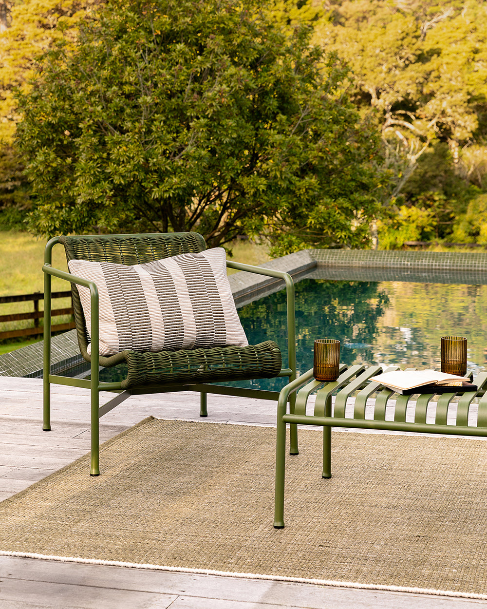 Baya Solar Outdoor Lumbar Cushion in Mangrove, styled on an outdoor sofa beside a pool.