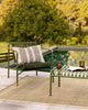Baya Solar Outdoor Lumbar Cushion in Mangrove, styled on an outdoor sofa beside a pool.