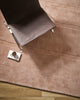 Baya Strata NZ wool floor rug in Clay, overhead view beneath a leather chair with a coffee cup on a saucer, on a timber floor.