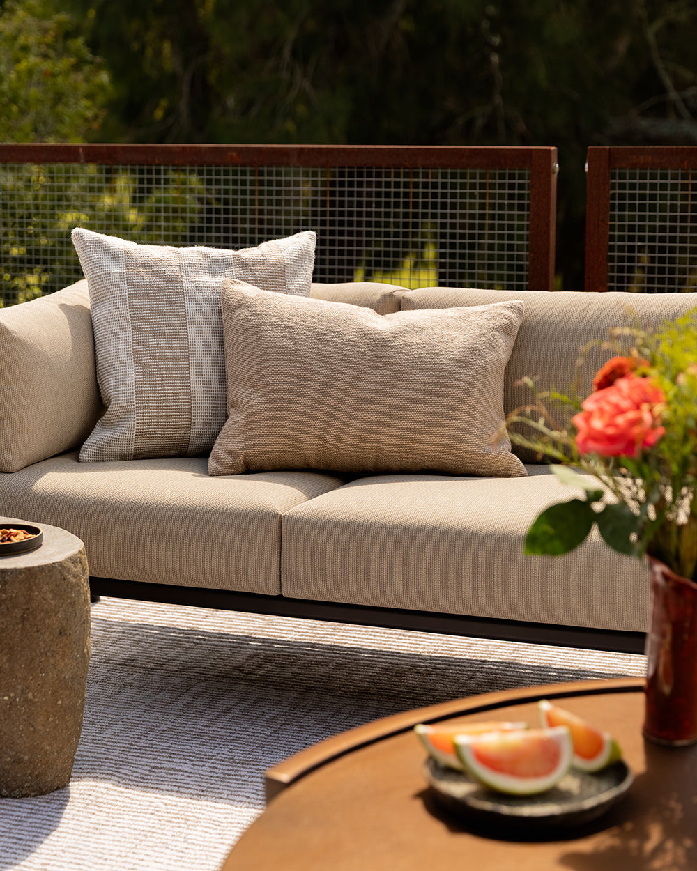Baya Tide Outdoor Cushion in Almond styled on an outdoor sofa, a closer view beside a grey patterned cushion.