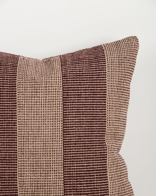 Close-up of the Baya Tide Outdoor Cushion in Claret, showing the woven linework stripe and piped edge.