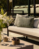 Baya Tide Outdoor Cushion in Eucalyptus styled on an outdoor sofa, a closer view with white lilies in the foreground.