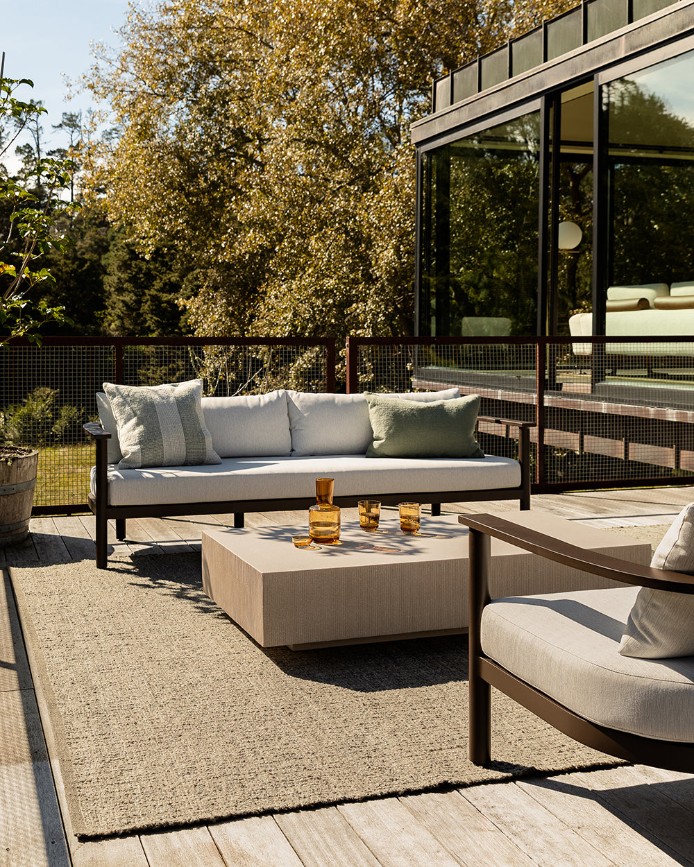 Baya Tide Outdoor Cushion in Eucalyptus styled on an outdoor sofa on a deck, with a lounge chair and coffee table.