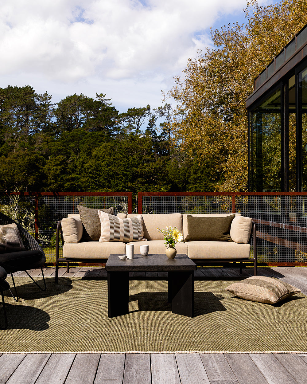 Baya Tide Outdoor Cushion in Mangrove styled on an outdoor sofa, a closer view with flowers and cups.