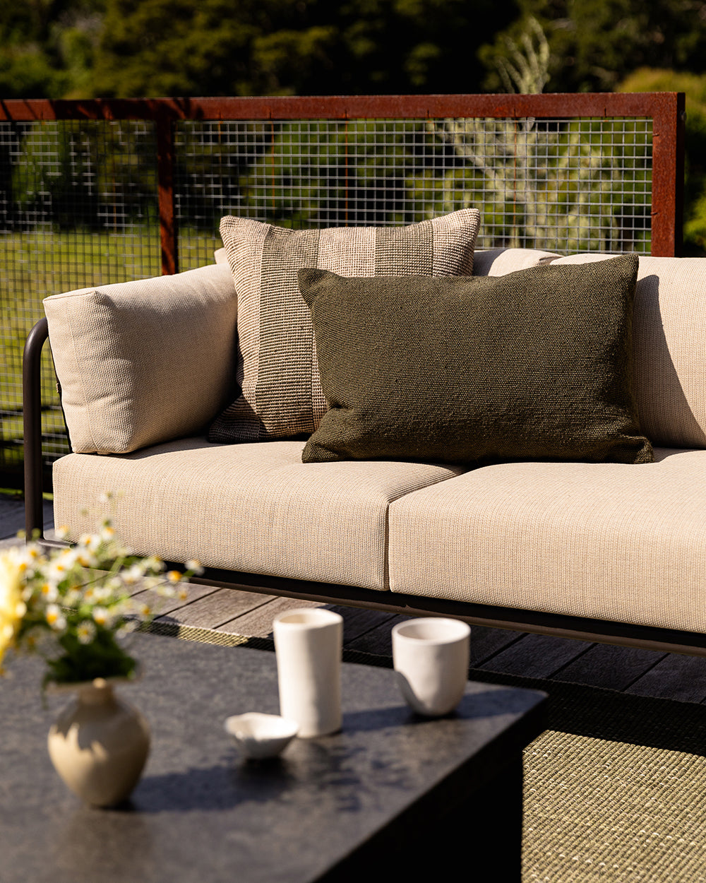 Baya Tide Outdoor Cushion in Mangrove styled on an outdoor sofa with a matching armchair and a jute-look rug.