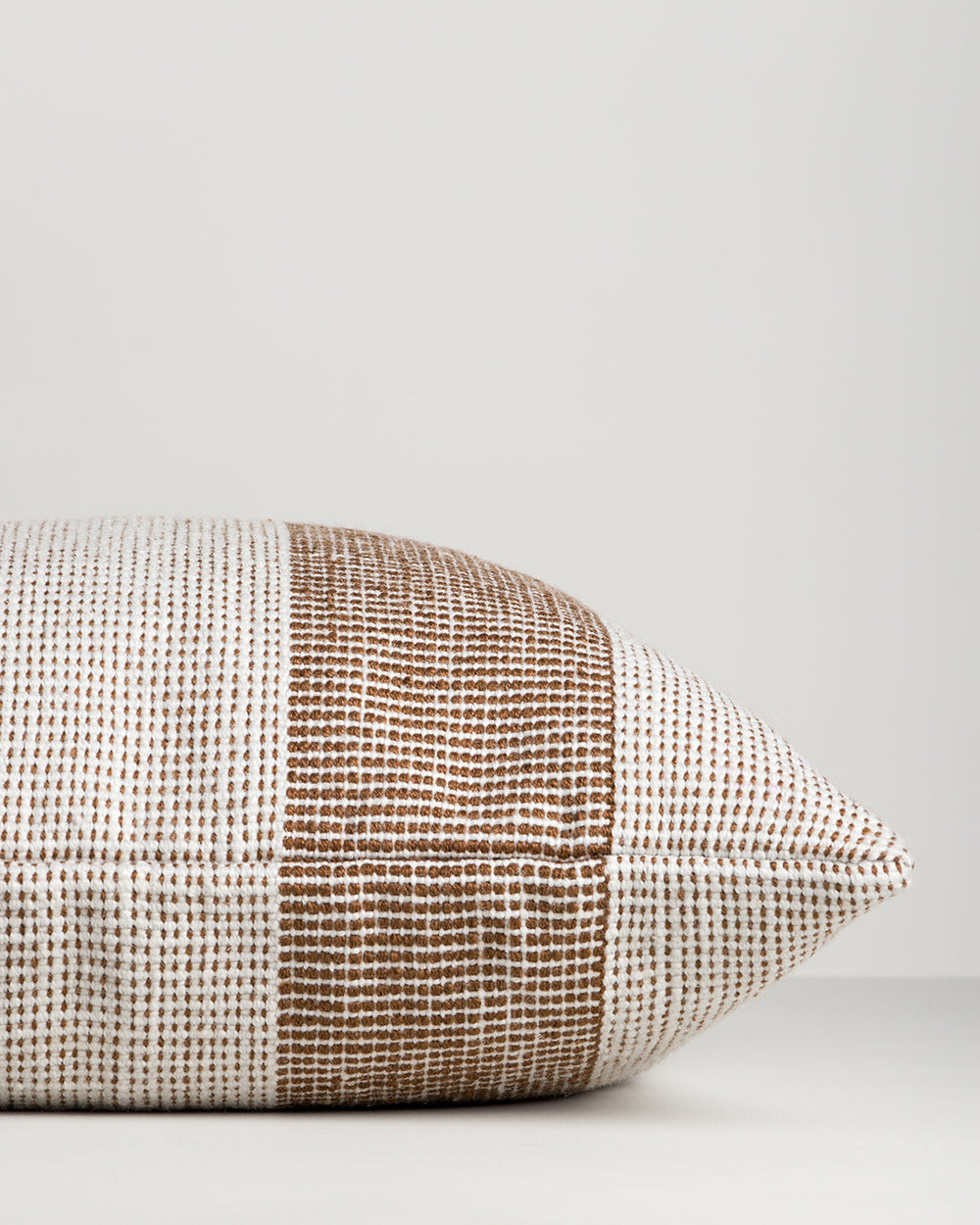 Side view of the Baya Tide Outdoor Cushion in Tobacco, showing the handwoven stripe wrapping the cushion edge.