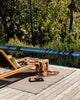 The Rhodes Teak Outdoor rug by Baya, seen under a lounger on the deck of a contemporary home
