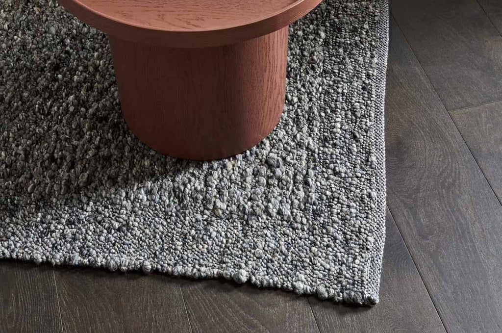 A textural wool blend boucle style rug by Globe West and Soren Liv NZ in shades of grey and charcoal, situated under a coffee table. 