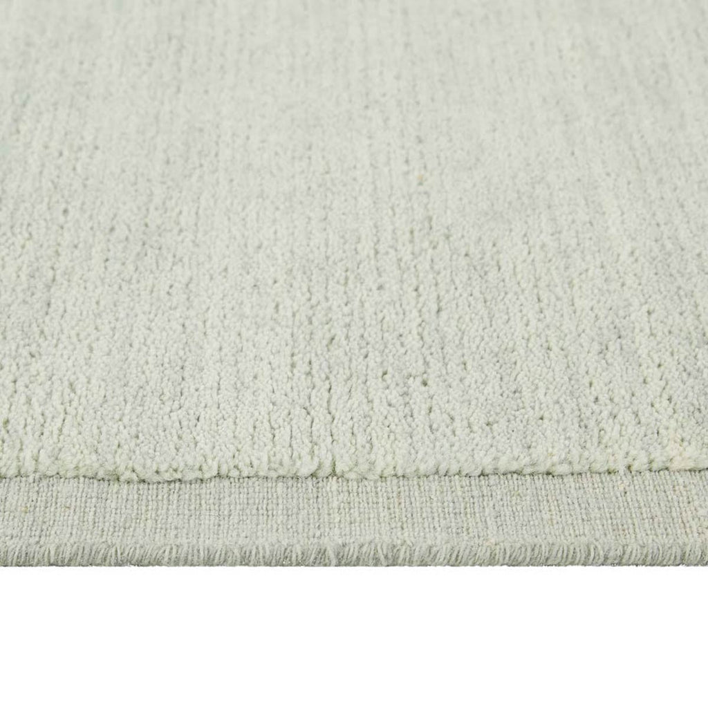 Close up of the weave of a handmade, 100% wool floor rug by Soren Liv NZ and Globe West, in subtle shades of light blue and green, shades of seafoam. The edge is indented, lending interest to the rug. 