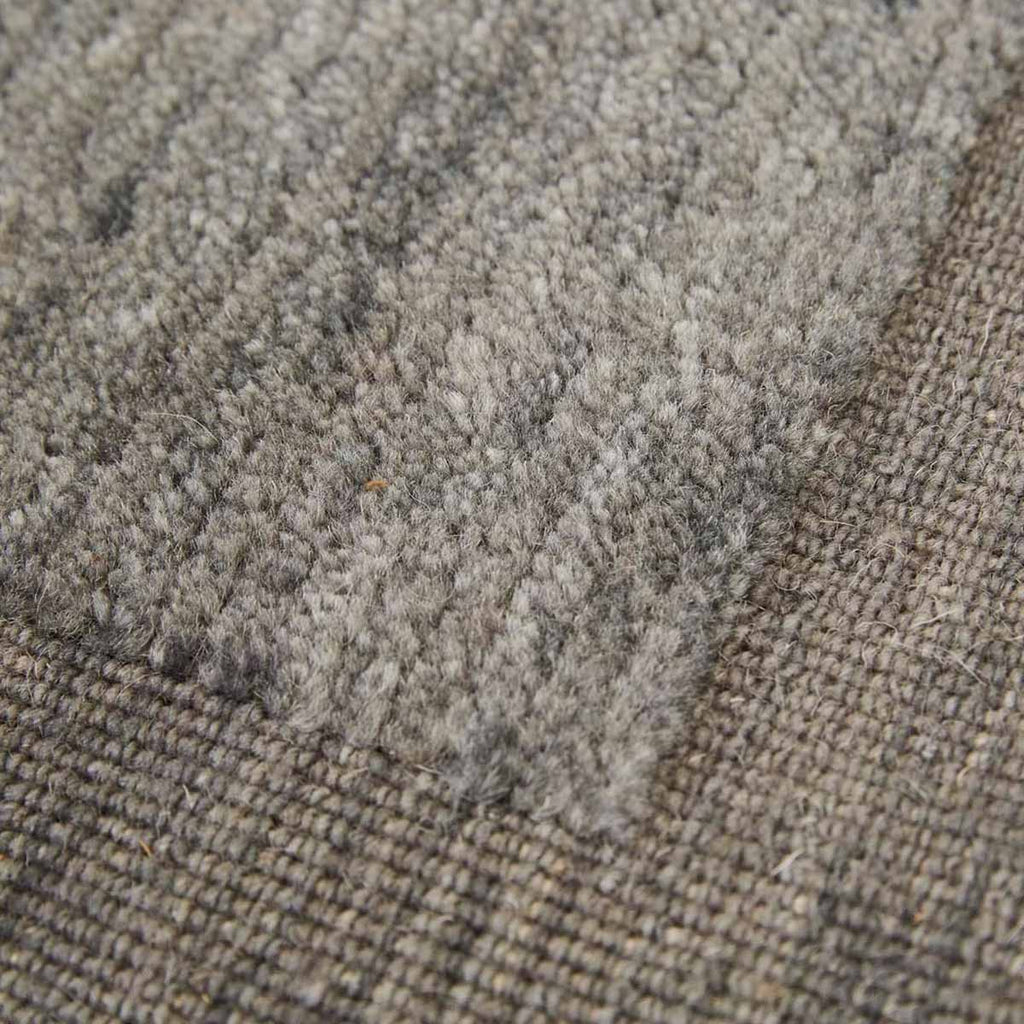 Close up view of a handmade wool rug by Globe West and Soren Liv, in a neutral, muted blue shade, with an indented border adding interest. 