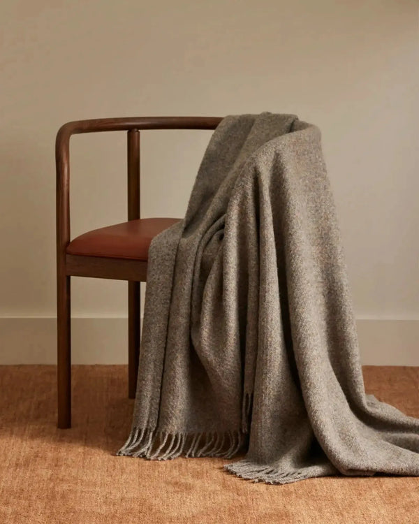 Brown recycled wool throw blanket with fringe, draped over a chair