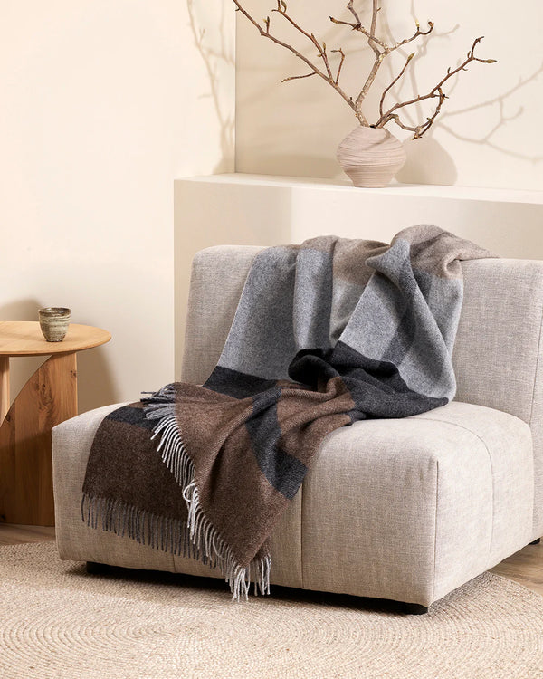 Baya Brunswick nz wool plaid throw in greys, blacks and browns draped over a cream chair