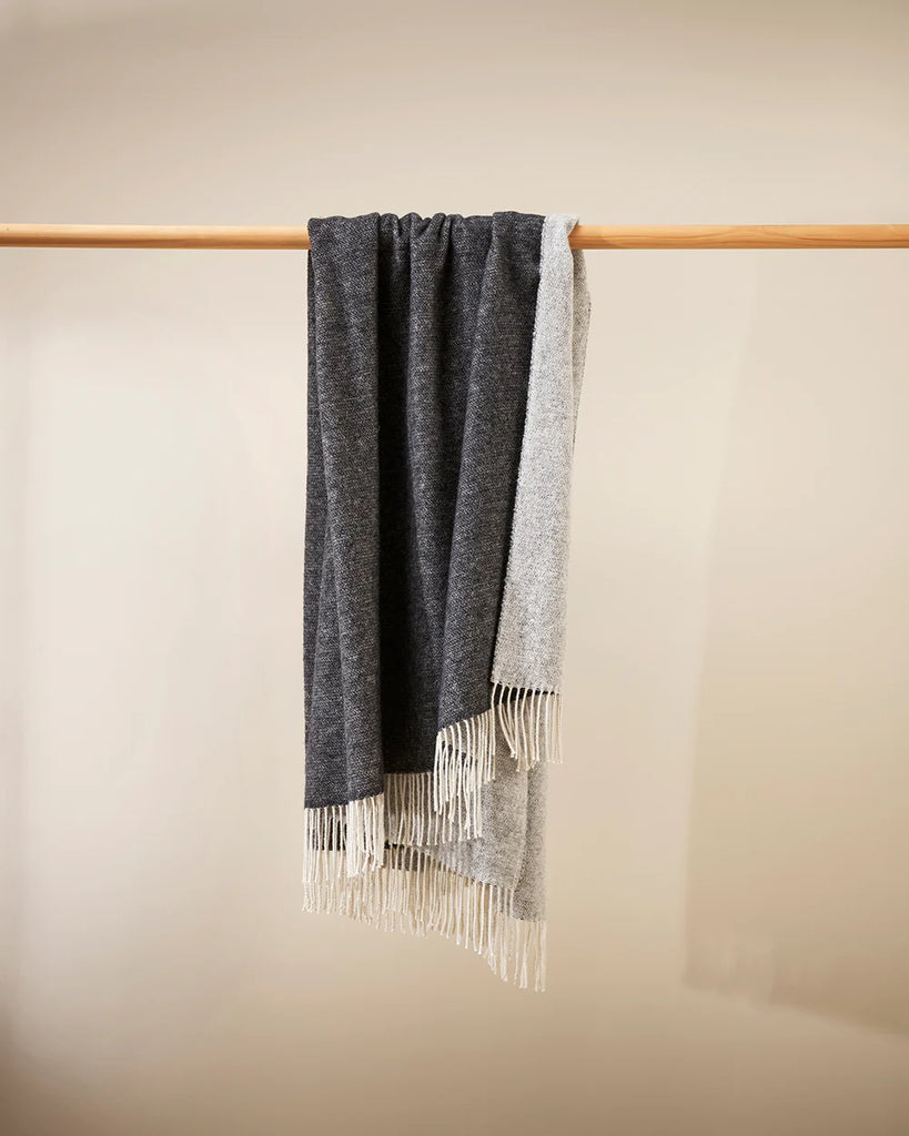 A two-toned charcoal and grey merino blend throw by Baya draping over a rail