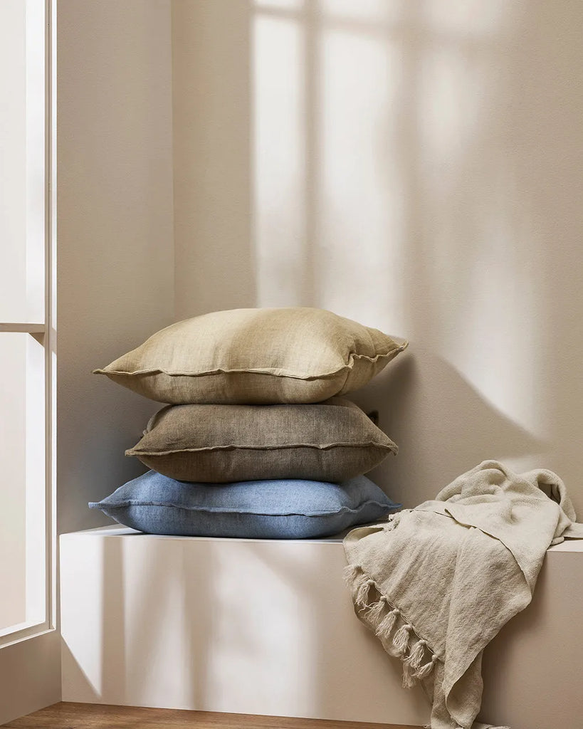 Baya contemporary linen cushions stacked on a window seat next to a linen throw