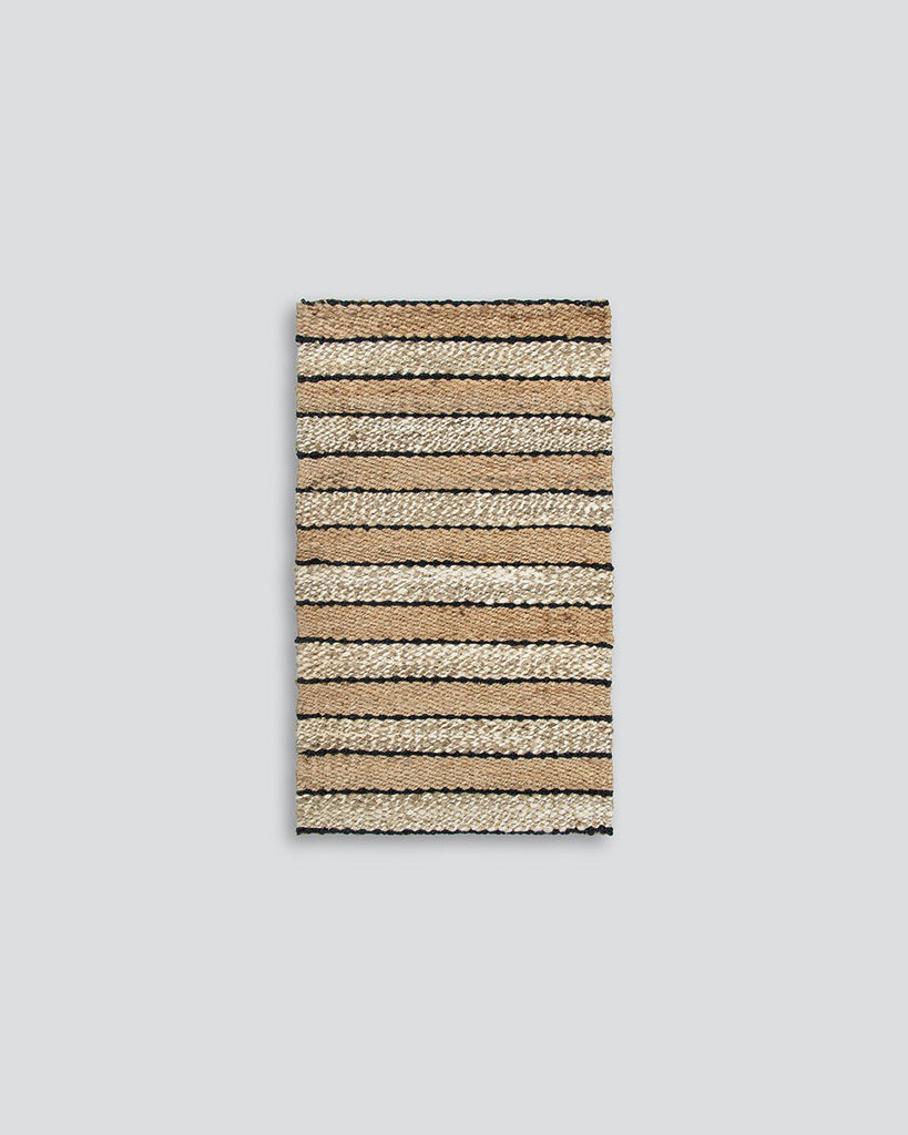 A full image of a striped doormat in different tones of natural jute, handwoven and designed by Baya. 