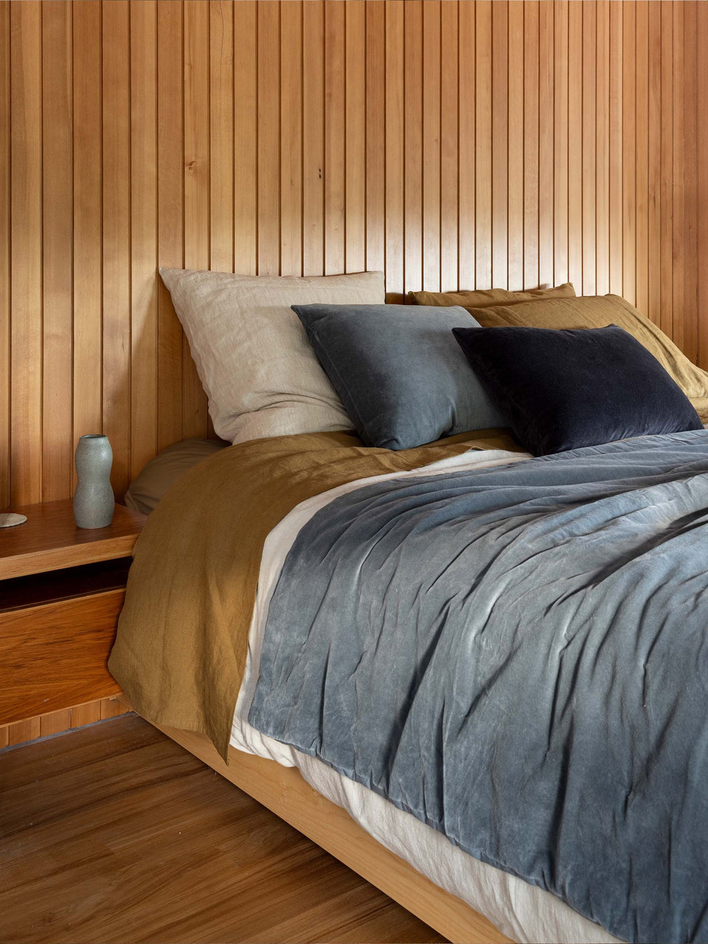 Città Cotton Velvet Quilt in Cod on a bed in a timber-panelled bedroom, layered with linen bedding