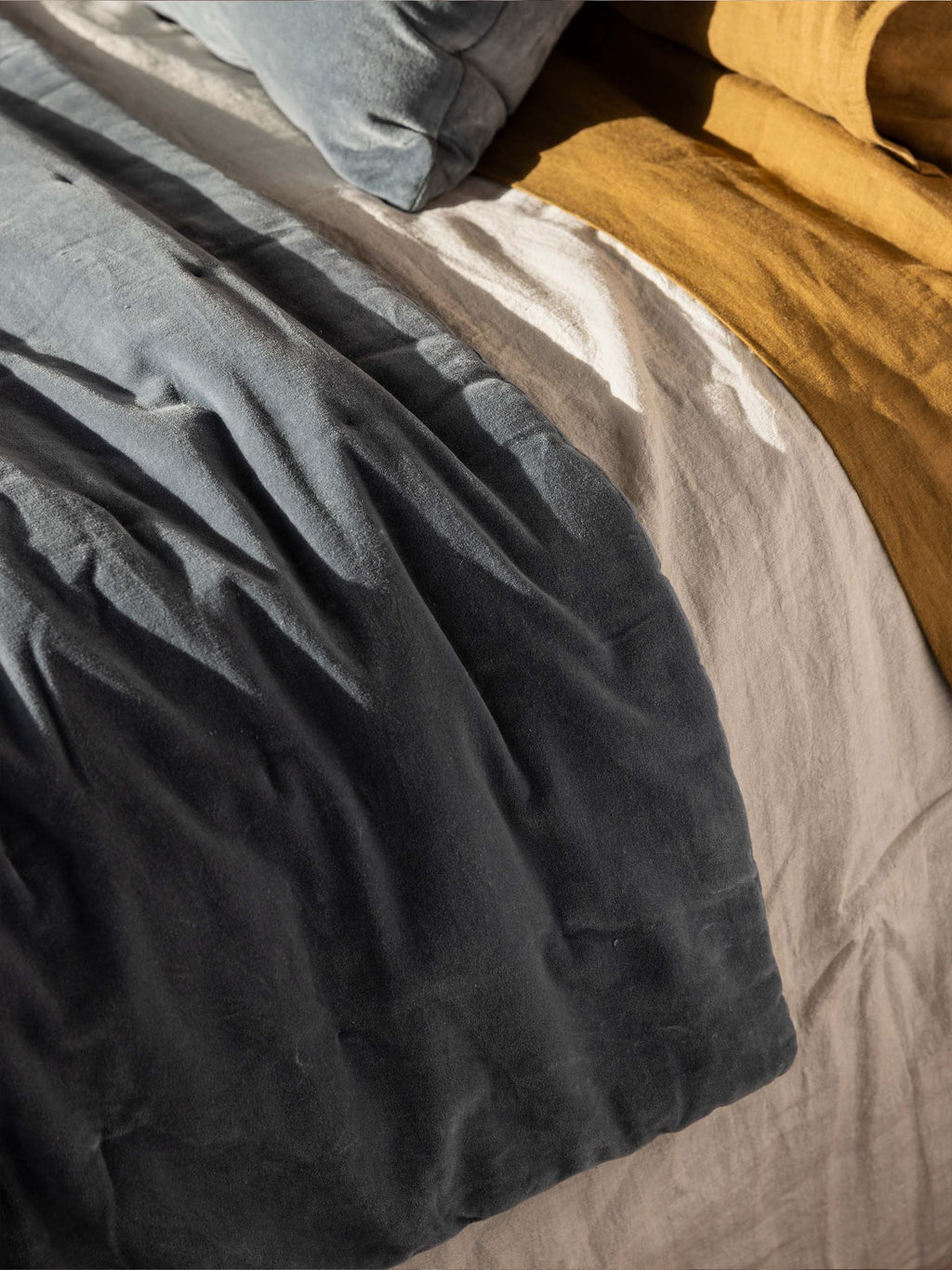 Città Cotton Velvet Quilt in Cod folded across a bed with natural and ochre linen bedding