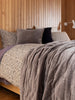 Città Cotton Velvet Quilt in Doe, draped over the end of a bed in a styled bedroom.