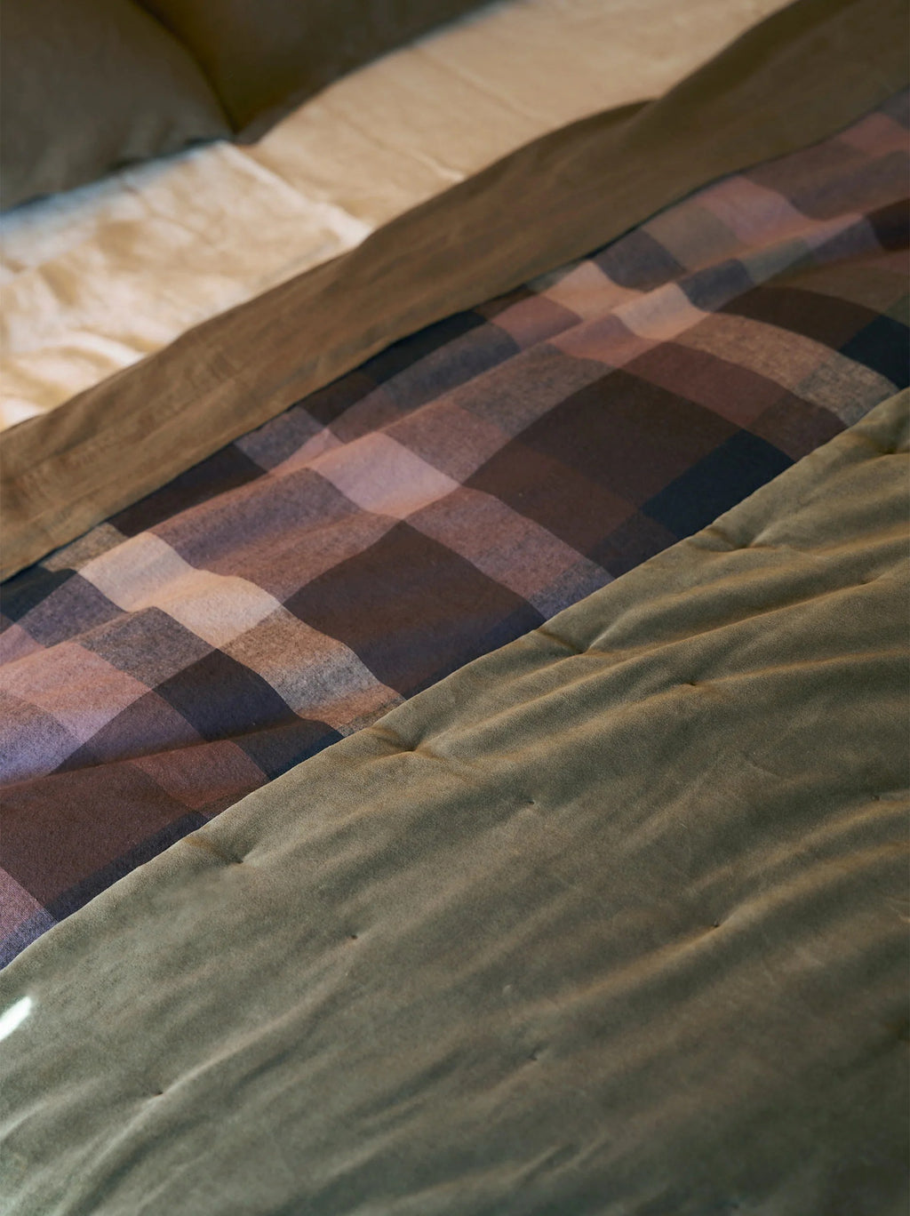 Città Cotton Velvet Quilt in Ivy on a bed, layered with a checked wool blanket and linen bedding
