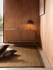 Città Joni Wool Mat in Kelp/Umber, styled in a wood-panelled living space.