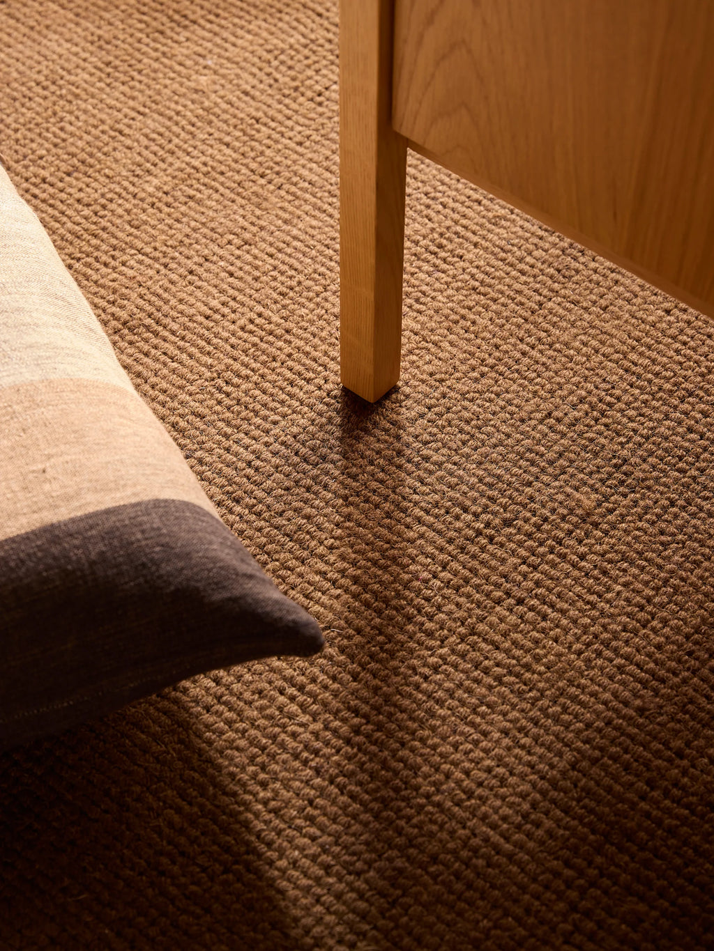 Città Joni Wool Mat in Kelp/Umber, styled beside a wooden table leg.