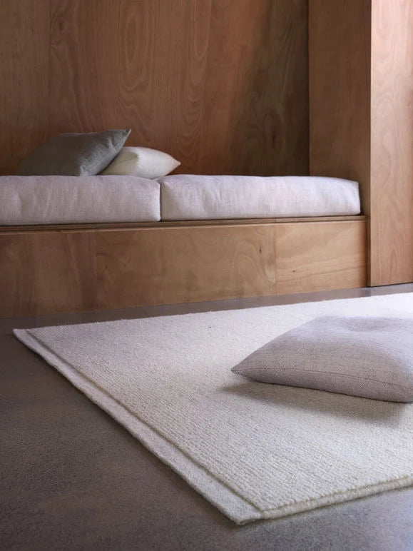 Città Joni Wool Mat in Oatmeal, styled beside a built-in bench on a concrete floor.